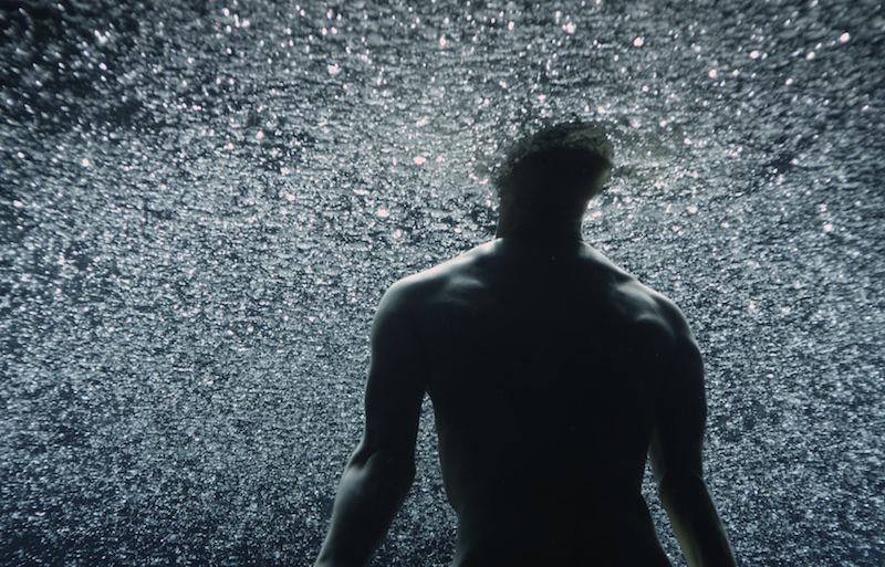 A shirtless man faces a sparkly background
